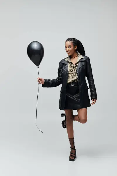 A chic African American woman in her 20s playfully poses with a black balloon in a leather outfit, exuding style and edge — Stock Photo