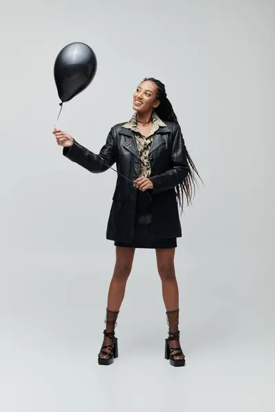 A black leather-clad African American woman with a black balloon exudes stylish confidence in her joyful pose — Stock Photo