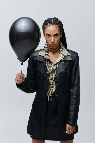 A young woman in a black leather jacket and animal print shirt poses with a black balloon. — Stock Photo