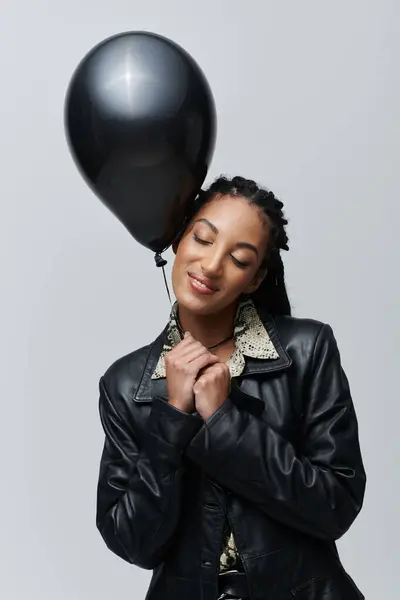 A young woman with a black balloon smiles gently, posing against a gray backdrop. — Stock Photo