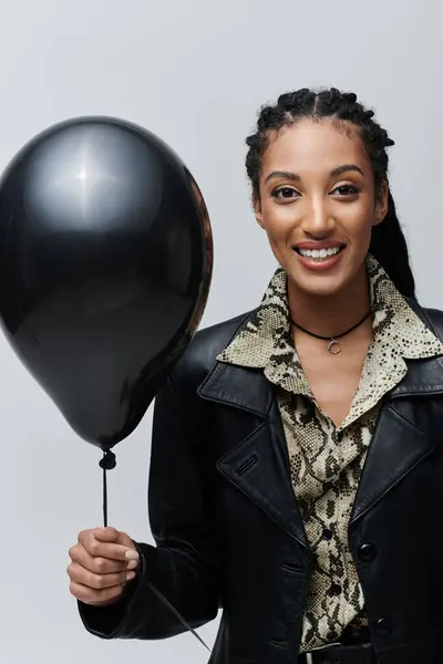 A young woman in a black leather jacket and animal print shirt smiles while holding a black balloon. — Stock Photo