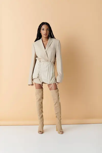 A young woman in a beige blazer and skirt poses confidently against a pale background, her long braids cascading down her back. — Stock Photo