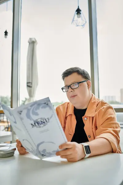 A man with Down syndrome sits at a cafe table, thoughtfully reading the menu. — Stock Photo