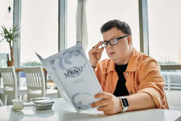 A man with Down syndrome sits at a cafe table, thoughtfully reviewing the menu before making a choice. — Stock Photo