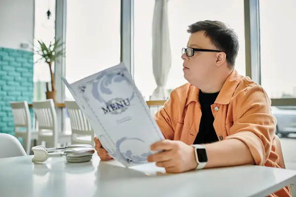 A man with Down syndrome sits at a cafe table, thoughtfully reading the menu and deciding what to order. — Stock Photo