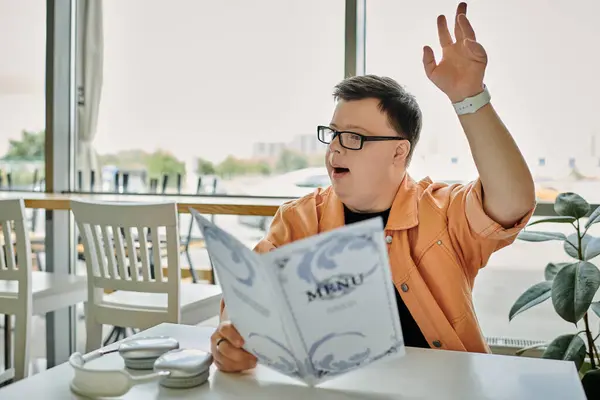 A man with Down syndrome enthusiastically raising hand and holding menu in a cafe. — Stock Photo