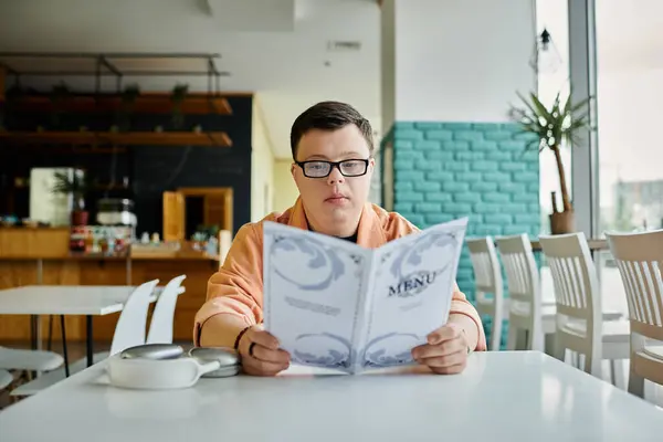 Un hombre con síndrome de Down examina cuidadosamente las opciones de menú en un café, disfrutando de una experiencia relajante e inclusiva. - foto de stock