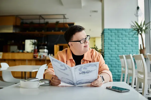 A man with Down syndrome sits at a cafe table, thoughtfully browsing the menu, ready to enjoy a delicious meal. — Stock Photo