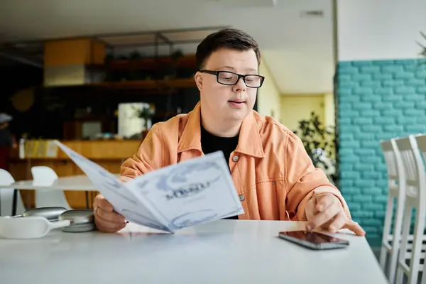Un hombre con síndrome de Down se sienta en una mesa de café, revisa cuidadosamente un menú y decide qué pedir. - foto de stock