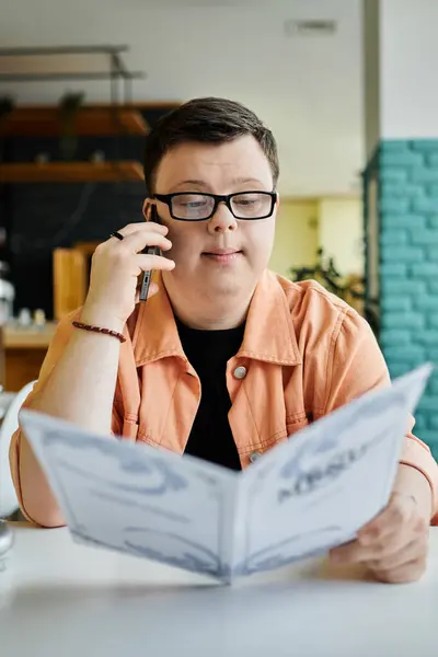 A man with Down syndrome sits at a cafe table, phone in hand, looking over the menu while deciding what to order. — Stock Photo