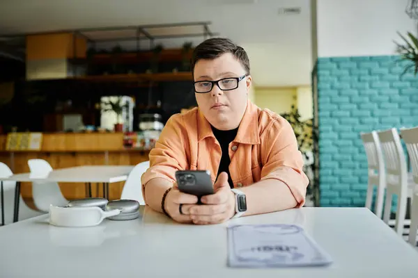 Ein Mann mit Down-Syndrom sitzt an einem Tisch in einem Café, schaut auf sein Telefon und überprüft die Speisekarte.. — Stockfoto