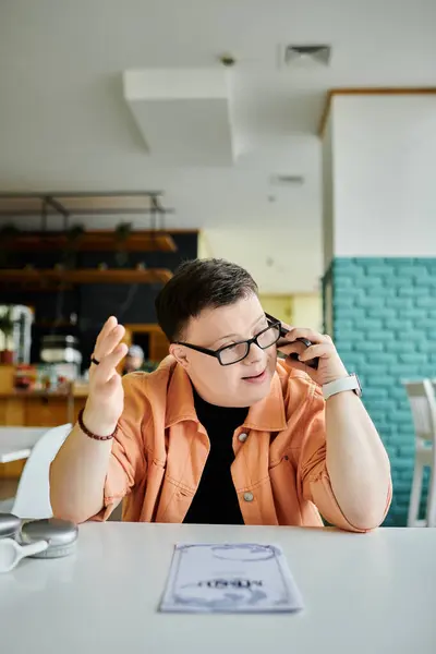 Un hombre con síndrome de Down hace una llamada telefónica mientras mira un menú en un café. - foto de stock