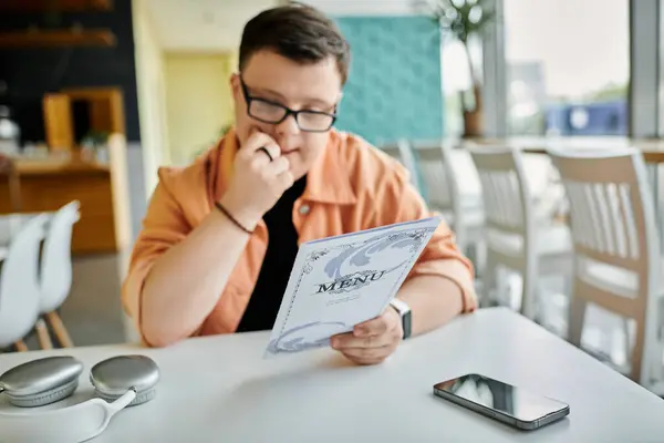 Ein Mann mit Down-Syndrom sitzt an einem Tisch in einem Café und betrachtet nachdenklich die Speisekarte. — Stockfoto