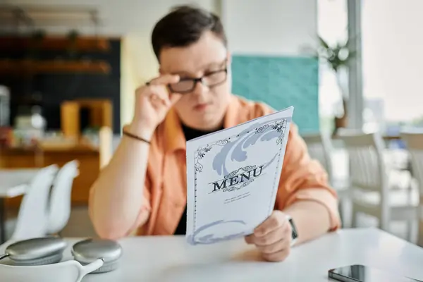 A man with Down Syndrome looks over the menu at a cafe, deciding what to order. — Stock Photo