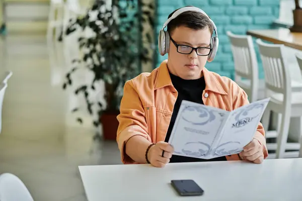 A man with Down Syndrome sits at a table in a cafe, thoughtfully reviewing the menu. — Stock Photo