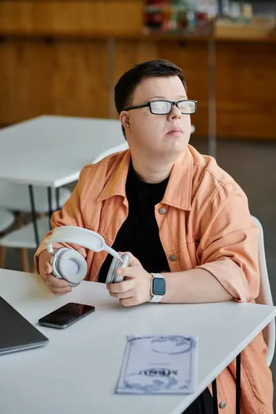 Ein Mann mit Down-Syndrom sitzt an einem Tisch in einem Café und hält ein Paar Kopfhörer. — Stockfoto