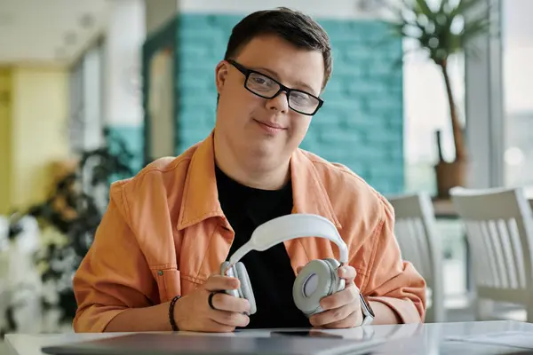 A man with Down syndrome sits in a cafe, wearing headphones, smiling and looking at the camera. — Stock Photo