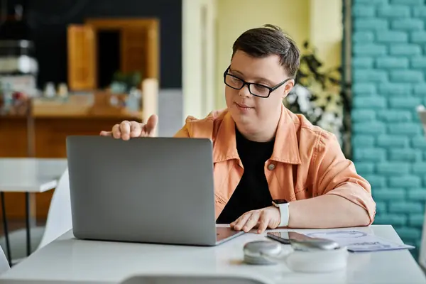 Un joven con Síndrome de Down está trabajando en su portátil en un café, centrado en su tarea. — Stock Photo