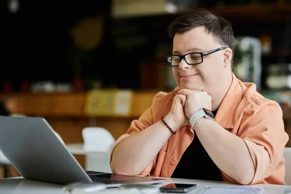 A man with Down syndrome sits in a cafe, thoughtfully working on his laptop. — Stock Photo