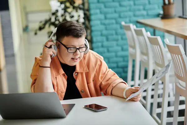 Un homme trisomique portant un casque travaille sur son ordinateur portable dans un café. — Photo de stock