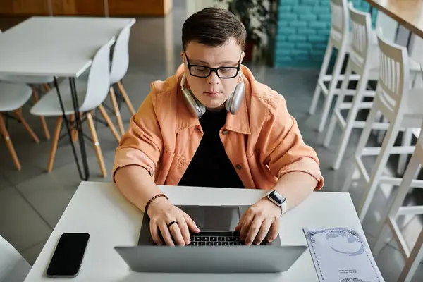 A man with Down syndrome sits at a cafe table, focused on his laptop. — Stock Photo