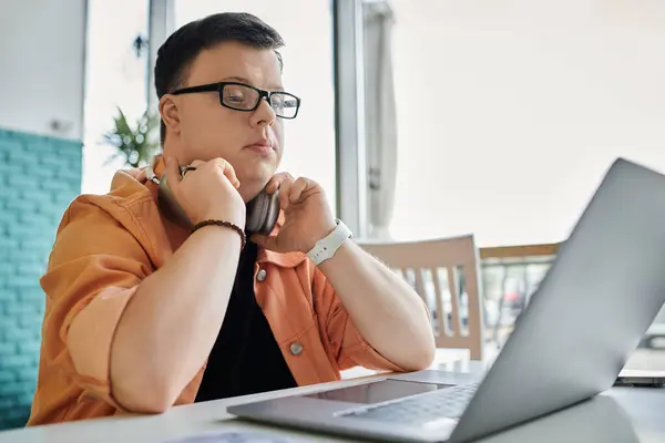 A man with Down syndrome sits at a table in a cafe, working on his laptop. — Stock Photo