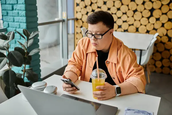 A man with Down syndrome works remotely on his laptop while enjoying a drink in a cafe. — Stock Photo