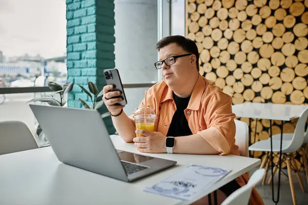 A man with Down syndrome uses his laptop and phone while enjoying a drink in a cafe. — Stock Photo
