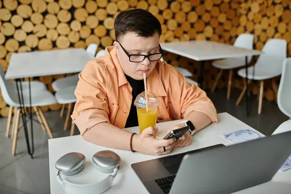Ein Mann mit Down-Syndrom genießt einen Drink, während er in einem Café an seinem Laptop arbeitet. — Stockfoto