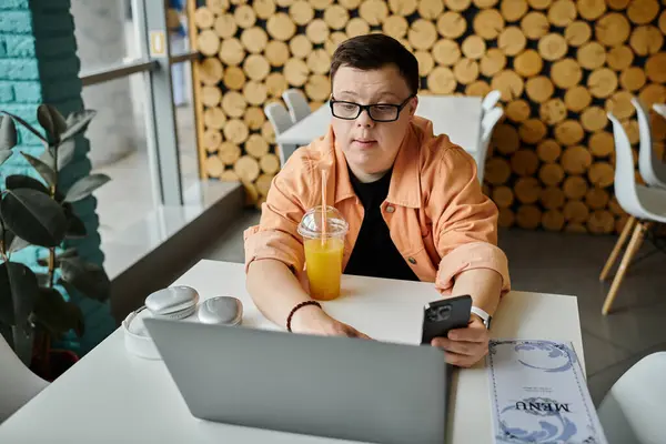 A man with Down syndrome works remotely on his laptop in a cafe, enjoying a drink. — Stock Photo