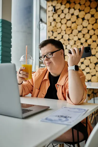 A man with Down syndrome sits in a cafe, working on his laptop while enjoying a beverage. — Stock Photo