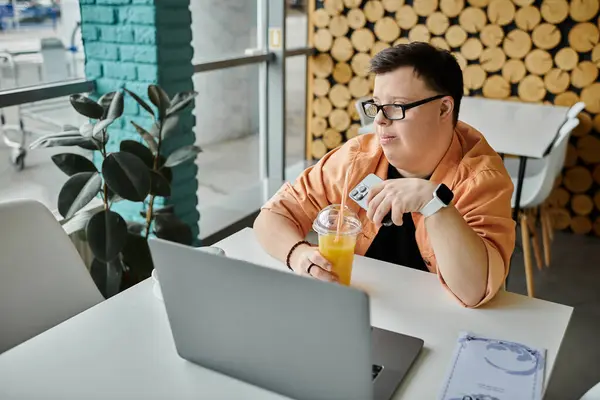 Un homme trisomique travaille à distance sur son ordinateur portable tout en prenant un verre dans un café. — Photo de stock
