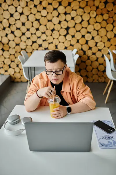 A man with down syndrome sits in a cafe, working on his laptop and enjoying a refreshing drink. — Stock Photo