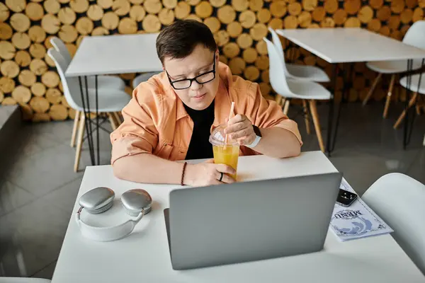 A man with Down syndrome works remotely on his laptop while enjoying a drink in a cafe. — Stock Photo