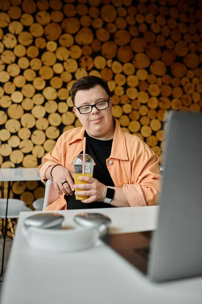 A man with Down syndrome enjoys a refreshing drink while working on his laptop at a cafe. — Stock Photo