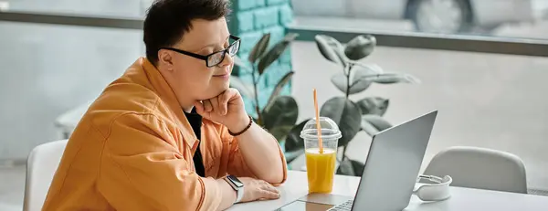 A man with Down syndrome sits in a cafe, working on his laptop, enjoying a glass of juice. — Stock Photo