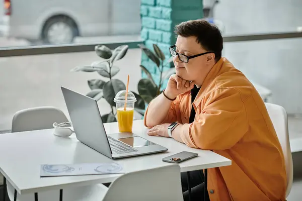 A man with Down syndrome works on his laptop at a table in a cafe, with a glass of juice beside him. — Stock Photo