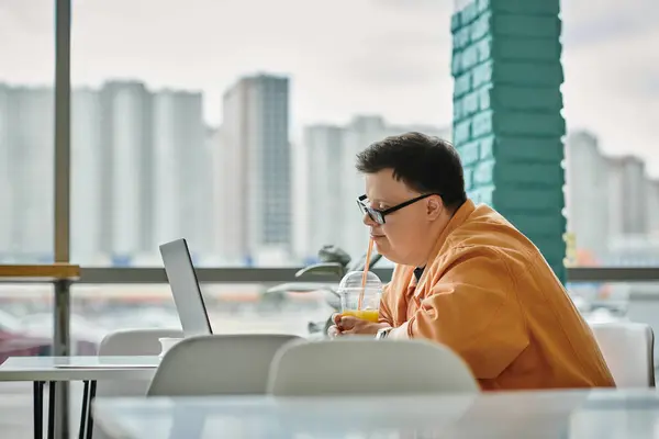 A man works remotely on his laptop in a cafe, enjoying a drink while taking in the city view. — Stock Photo