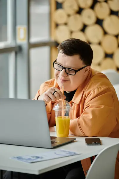 A man with Down syndrome sits in a cafe, sipping juice and working on a laptop. — Stock Photo