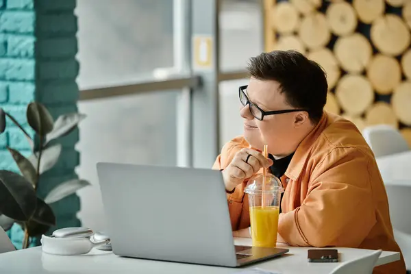A man with Down syndrome sits in a cafe, working on a laptop while enjoying a beverage. — Stock Photo