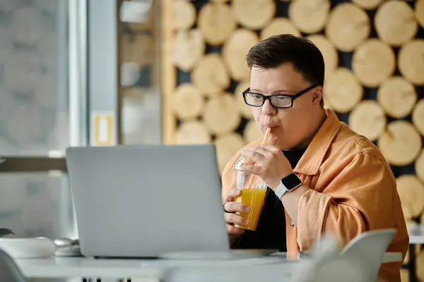 A man with Down syndrome sits in a cafe, working on his laptop while enjoying a refreshing drink. — Stock Photo