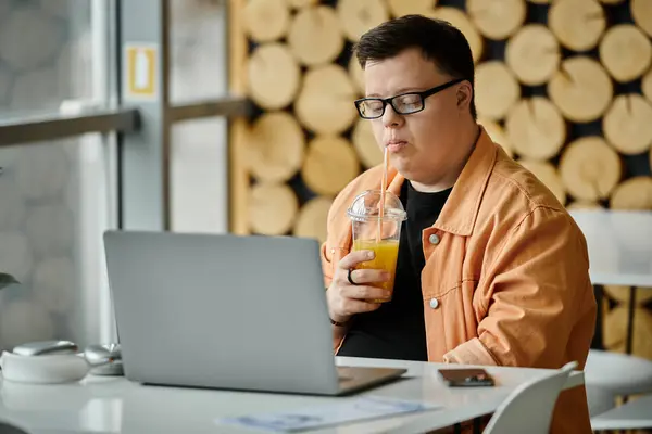 A man with Down syndrome sips on a beverage while working on his laptop at a cafe. — Stock Photo