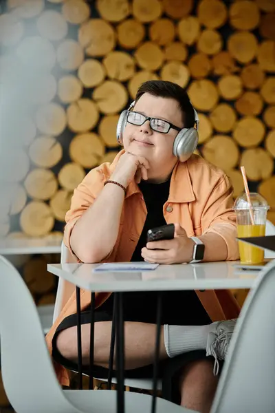 A man with Down syndrome sits in a cafe, headphones on and a phone in his hand, enjoying the day. — Stock Photo