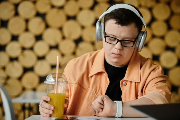 A man with Down syndrome works remotely on his laptop while enjoying a drink in a cafe. — Stock Photo