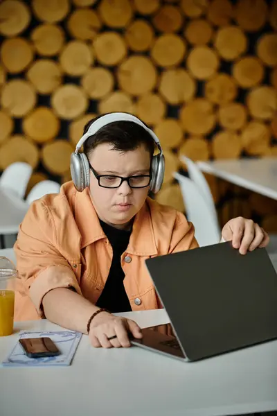 Ein junger Mann mit Down-Syndrom arbeitet mit Kopfhörern an seinem Laptop in einem Café. — Stockfoto