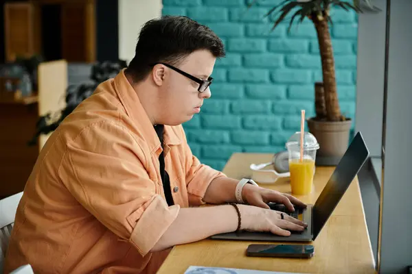 A man with Down syndrome works on his laptop in a cafe. — Stock Photo