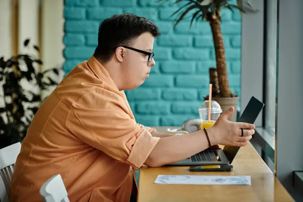 A man with Down syndrome works on a laptop in a cafe. — Stock Photo