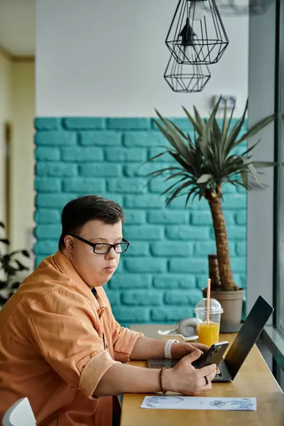A man with Down syndrome works on his laptop while enjoying a refreshing beverage at a cafe. — Stock Photo