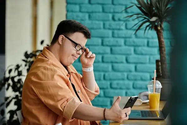 Un homme trisomique s'assoit à une table dans un café, travaillant sur son ordinateur portable. — Photo de stock