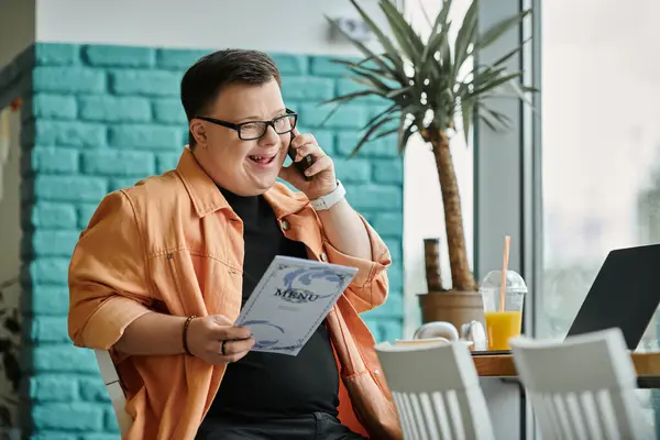 A man with Down syndrome smiles and talks on his phone while working remotely in a cafe. — Stock Photo